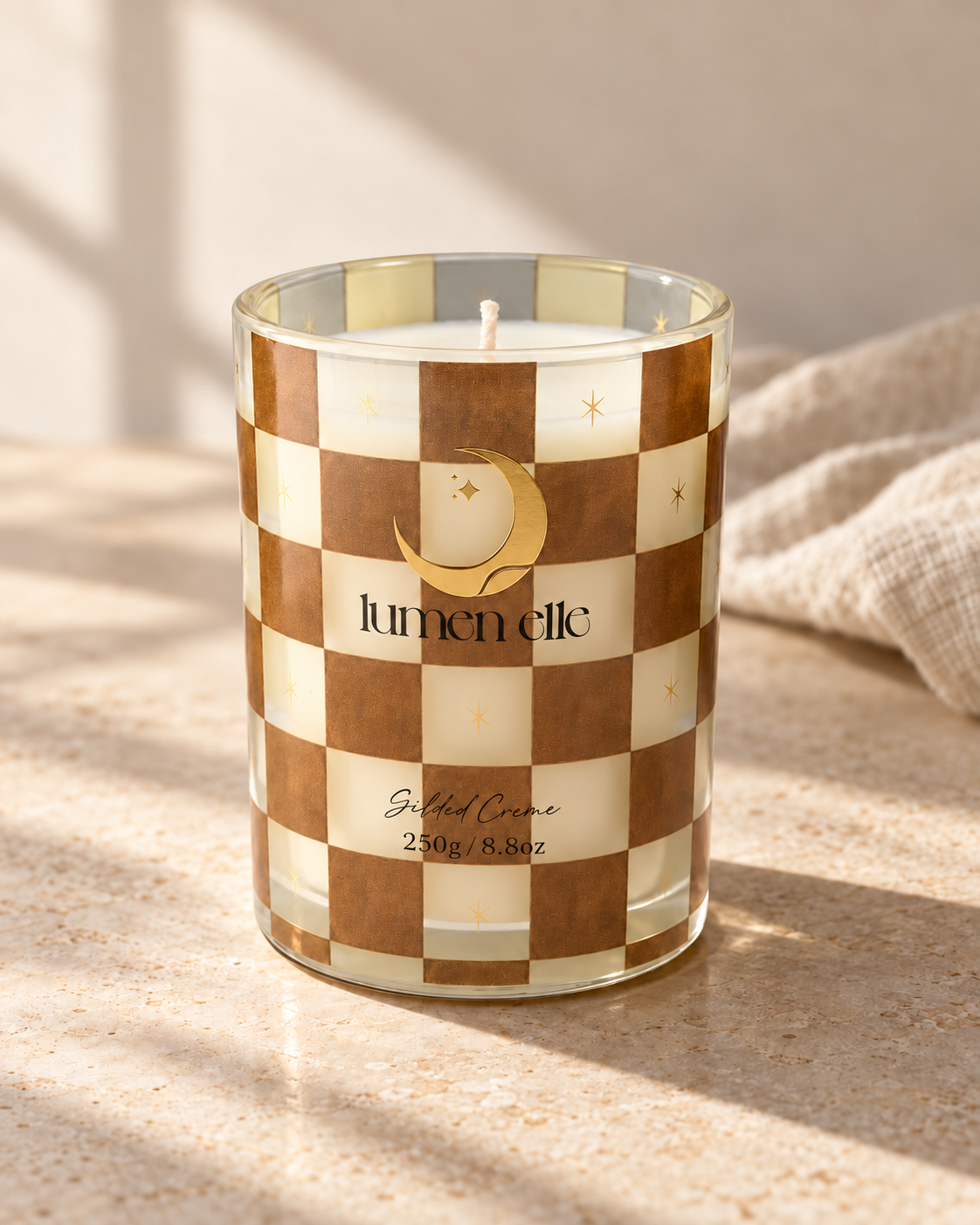 Lumenelle Gilded Créme checkered glass candle in warm natural light on limestone