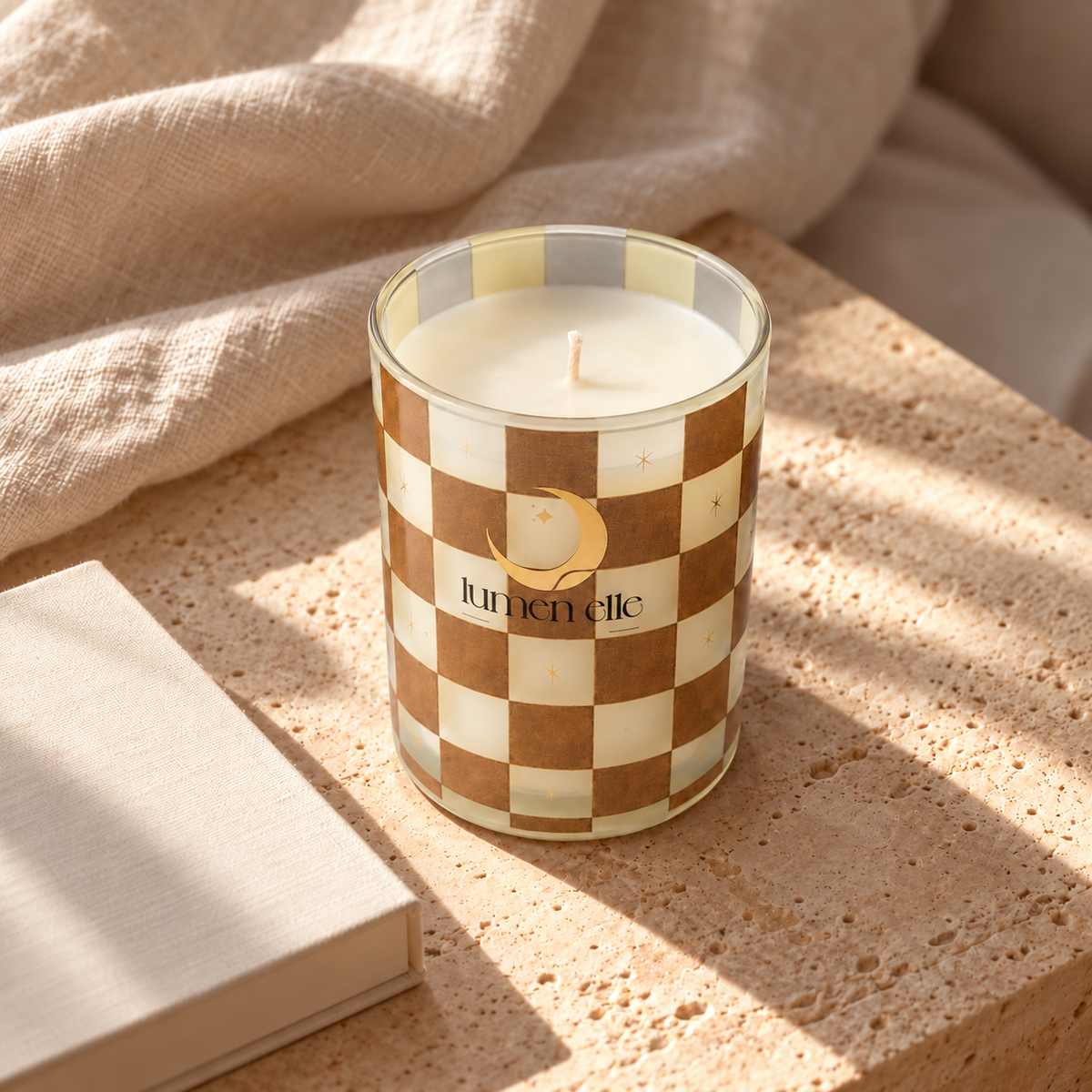 Lumenelle Gilded Crème candle beside a book and linen
