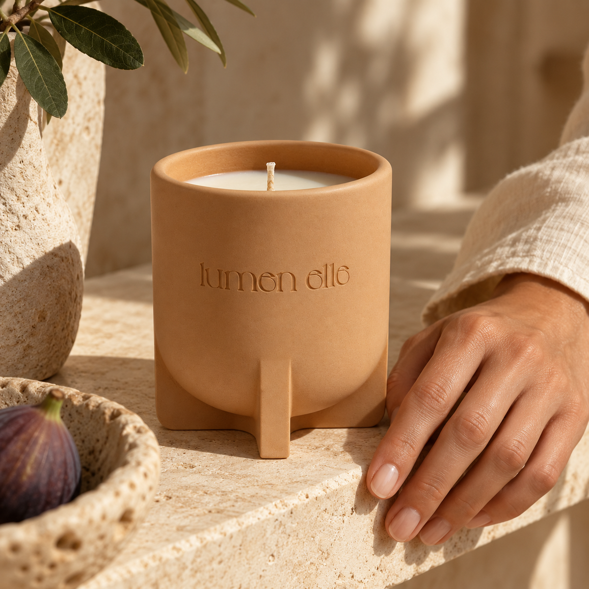 Lumenelle Mediterranean Fig candle on a stone shelf beside a hand